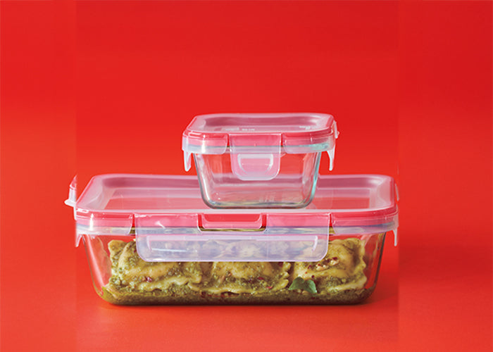 Stack of glass food containers with plastic lids on a red background