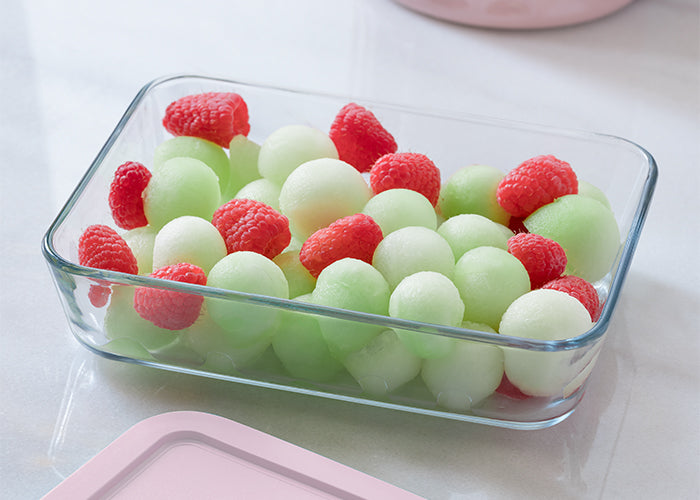 Glass container filled with green and red fruit on a white surface