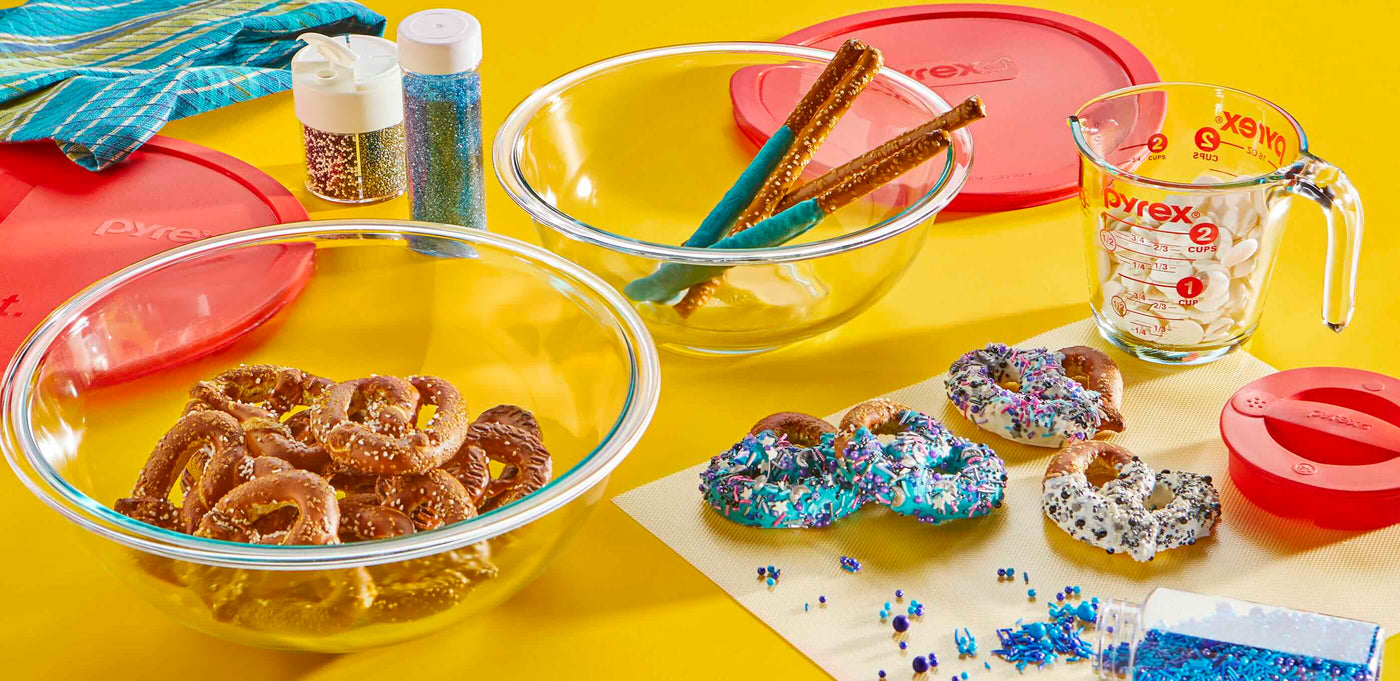Glass bowls with snacks, colorful sprinkles, and Pyrex measuring cups on a yellow background