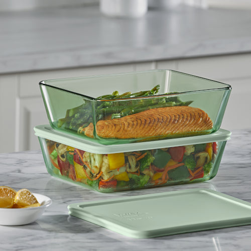 Glass food containers with salmon, asparagus, and mixed vegetables on a kitchen counter.
