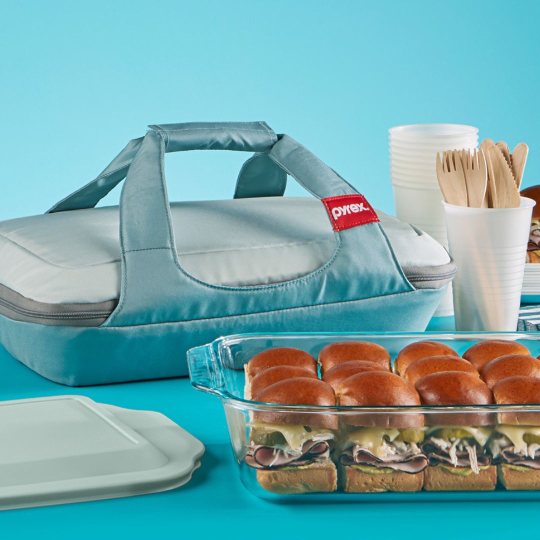 Pyrex baking dish with sandwiches and a carrying case on a blue background