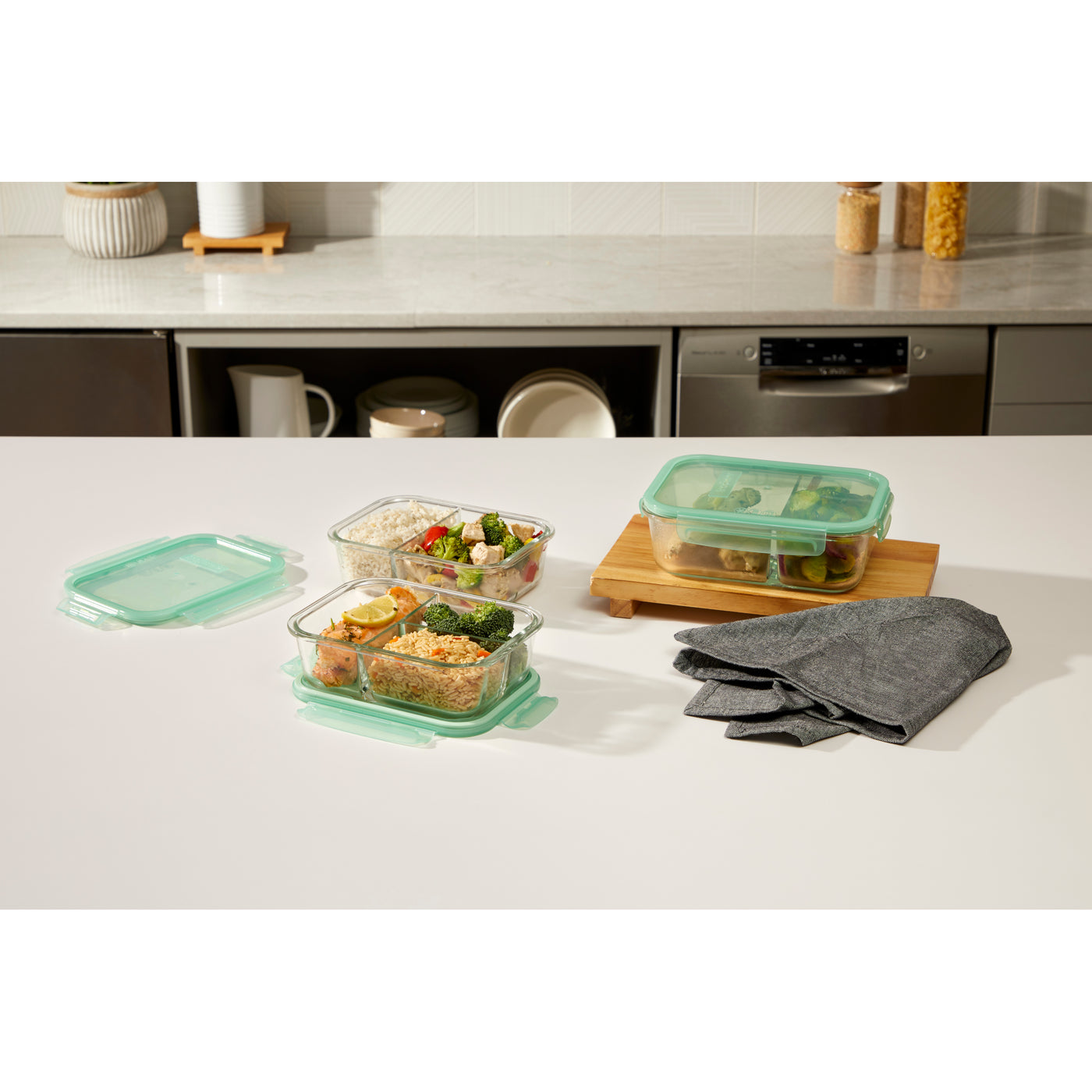 Glass meal prep containers with rice, vegetables, and chicken on a kitchen counter.