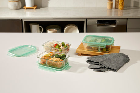 Glass meal prep containers with rice, vegetables, and chicken on a kitchen counter.