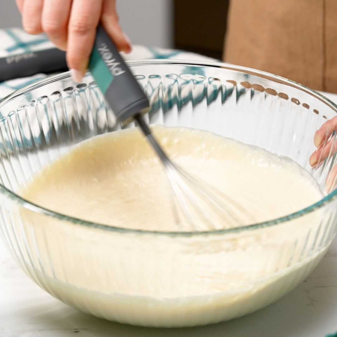 Person whisking batter in a glass bowl with a whisk.