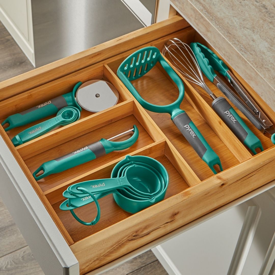 Kitchen utensils including a whisk, spatula, and measuring cups in a wooden drawer organizer.