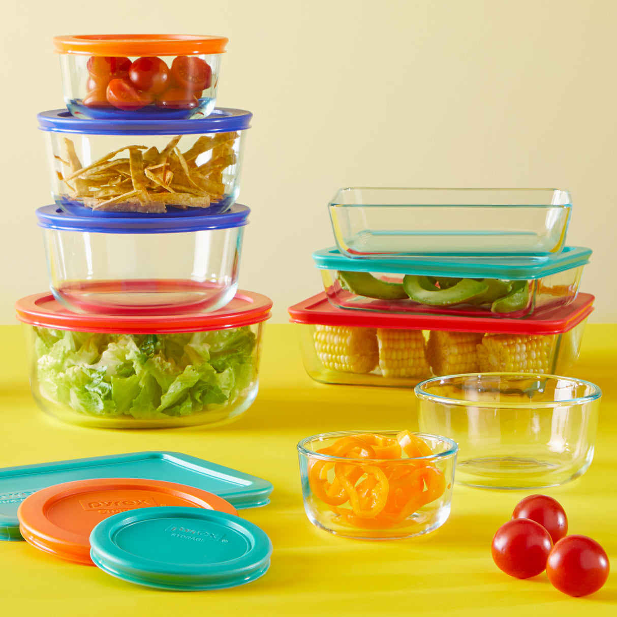 Set of glass food containers with colorful lids on a yellow background