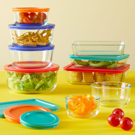 Set of glass food containers with colorful lids on a yellow background