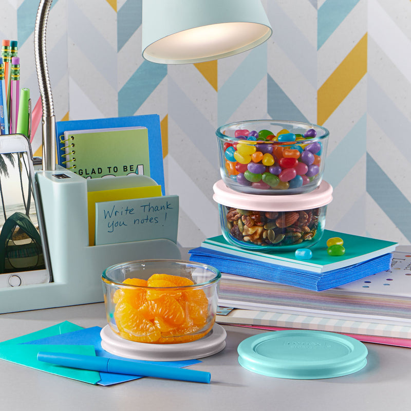 Glass storage bowls filled with jelly beans, nuts, and orange slices on a colorful desk.
