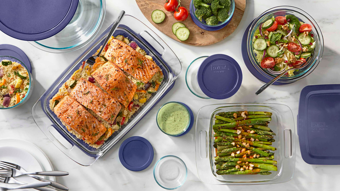Prepared meals in glass containers with purple lids on a white table.