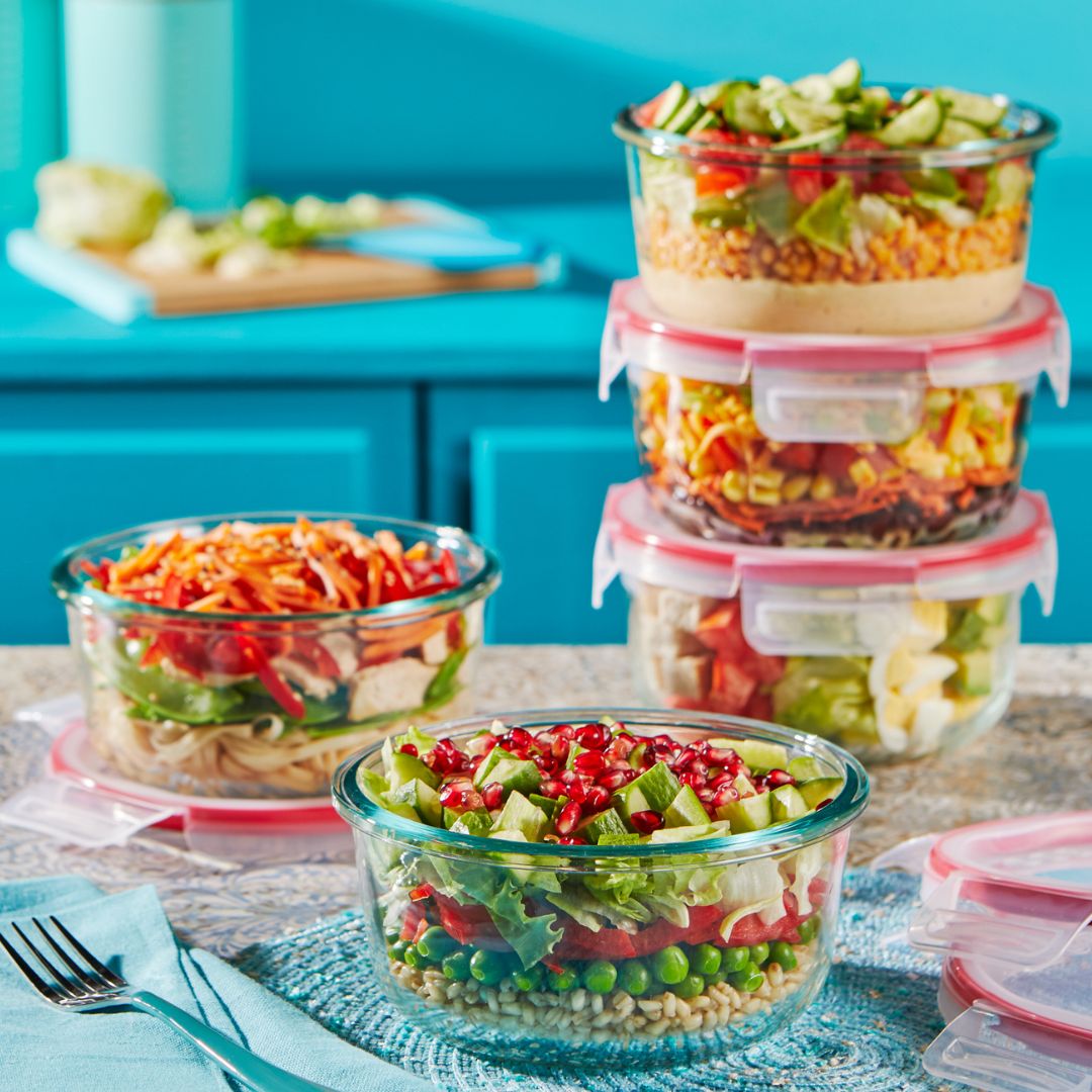 Glass containers with layered salads on a kitchen counter.