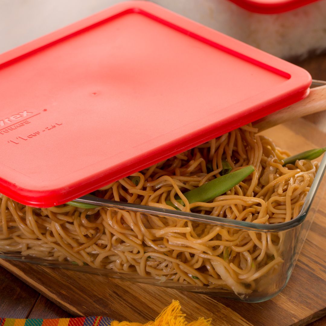 Glass container with red lid filled with noodles on a wooden surface