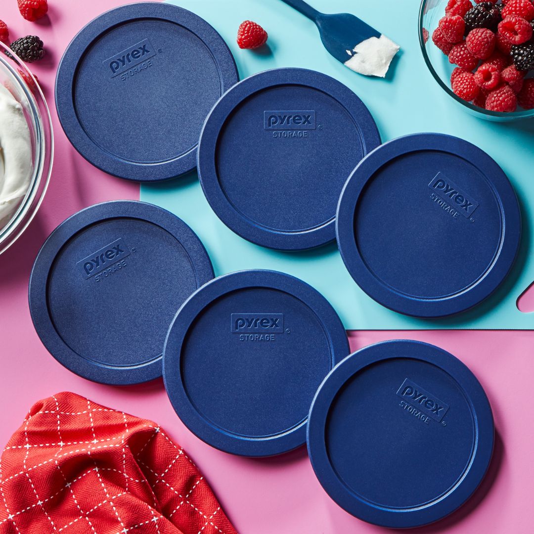 Pyrex blue storage lids on a colorful background with berries and a red cloth.