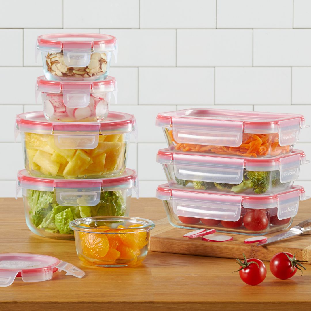 Set of glass food storage containers with pink lids on a wooden surface.