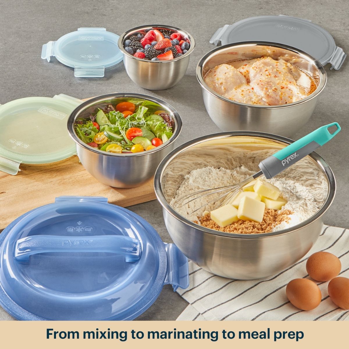 Set of stainless steel mixing bowls with lids on a kitchen counter, containing various food items.
