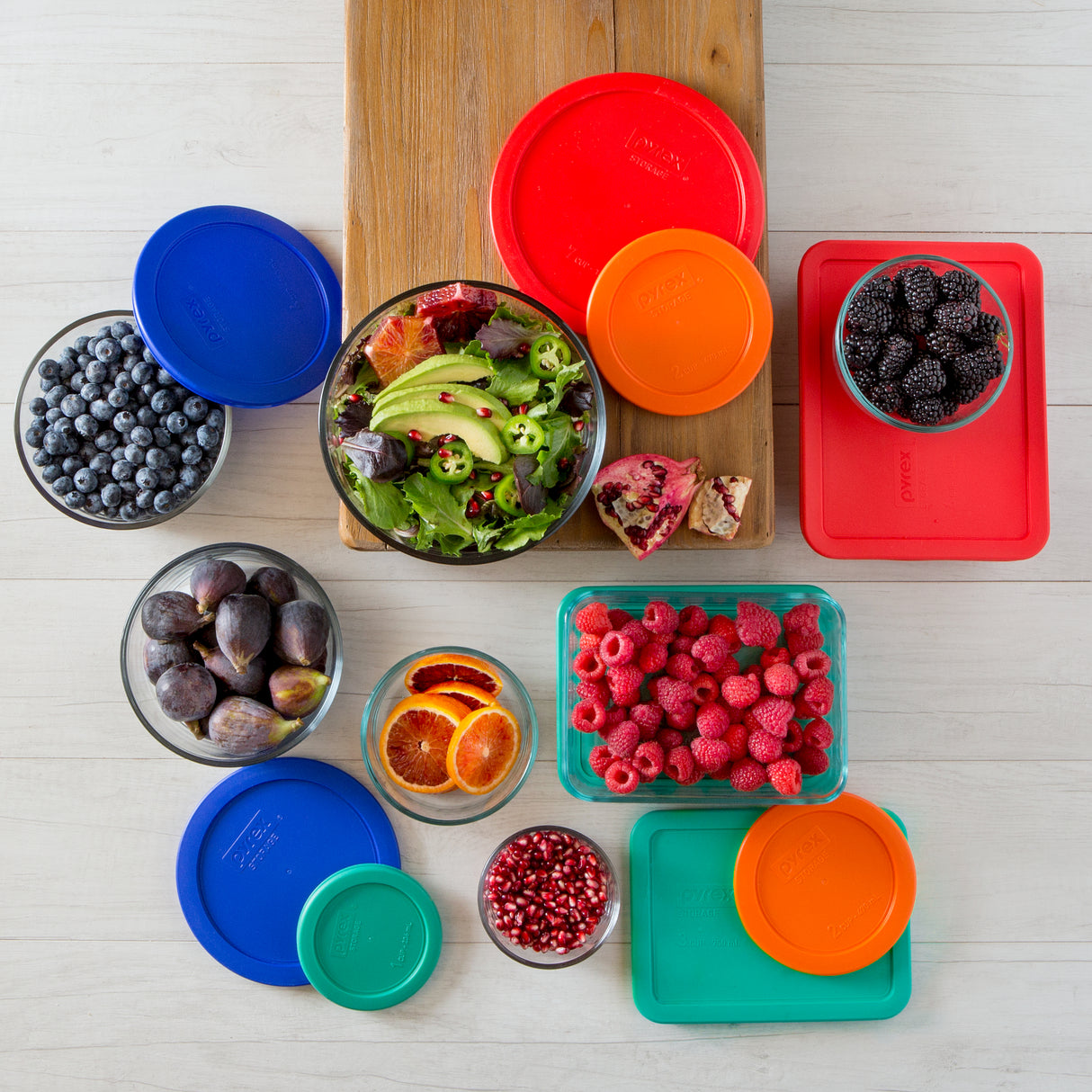 Assorted fruits and vegetables in containers with colorful lids on a wooden cutting board.