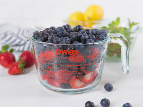 Measuring cup filled with mixed berries on a white surface.