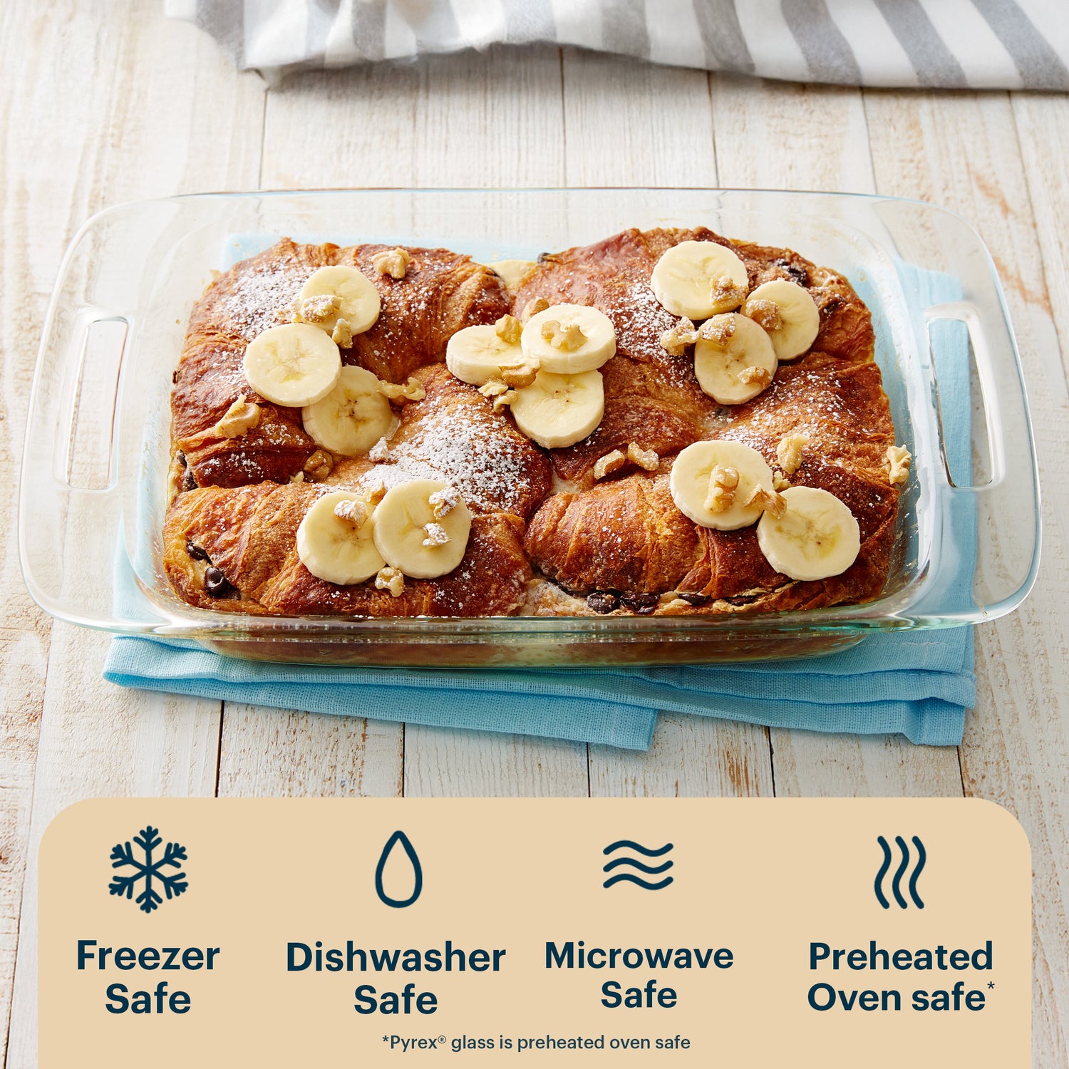 Baked dish with bananas and croissants in a glass dish on a wooden surface, with safety icons below.