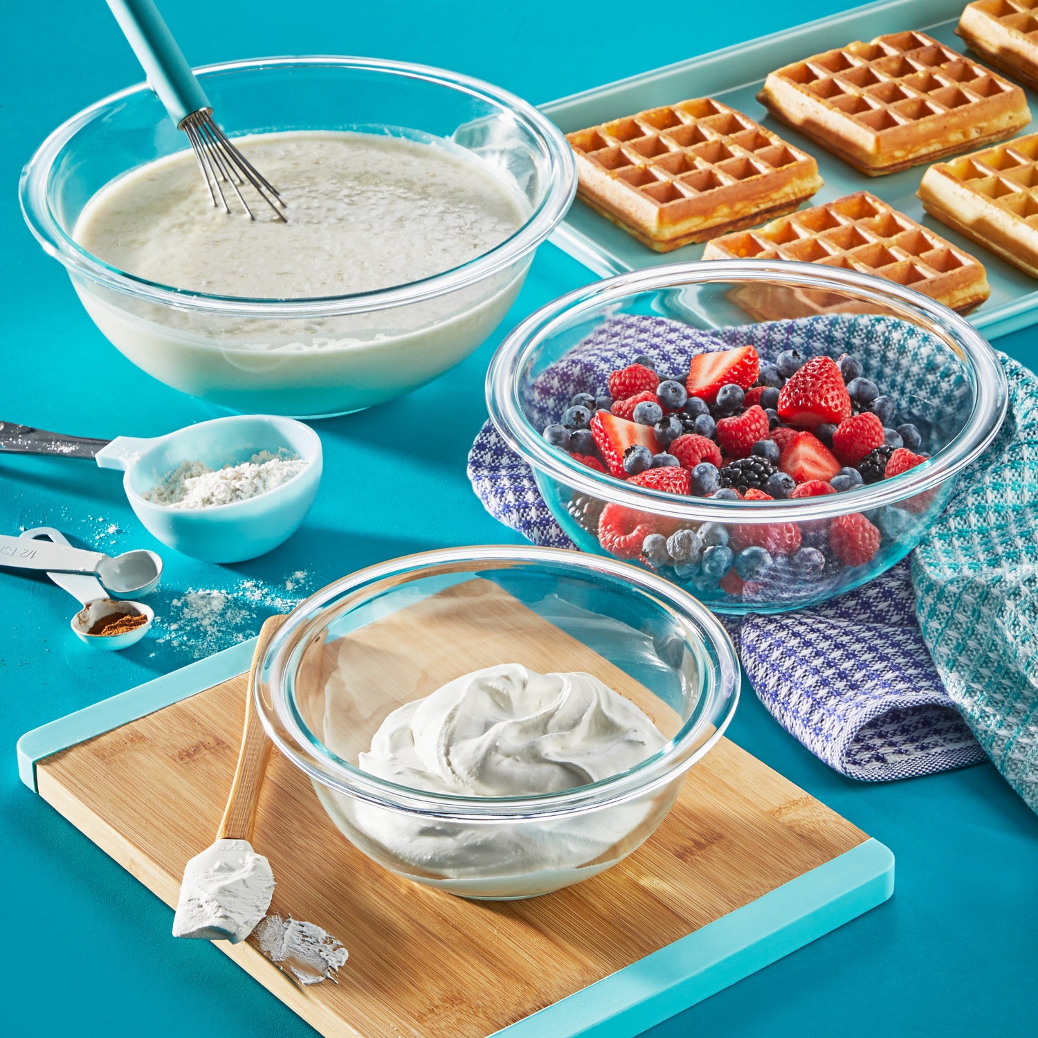 Baking setup with waffles, batter, and berries on a blue surface