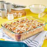 Glass dish with cinnamon rolls on a yellow tablecloth with mugs and bowls.