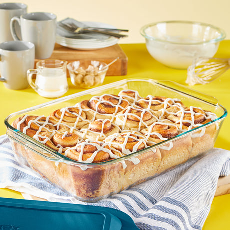Glass dish with cinnamon rolls on a yellow tablecloth with mugs and bowls.