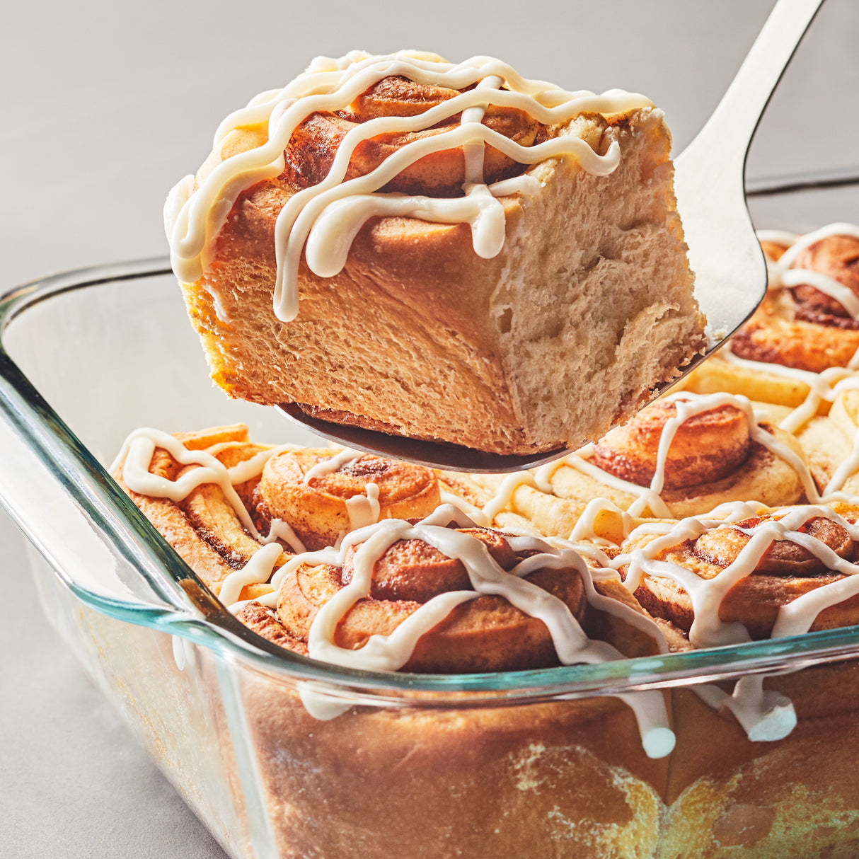 Cinnamon roll with icing being lifted from a baking dish