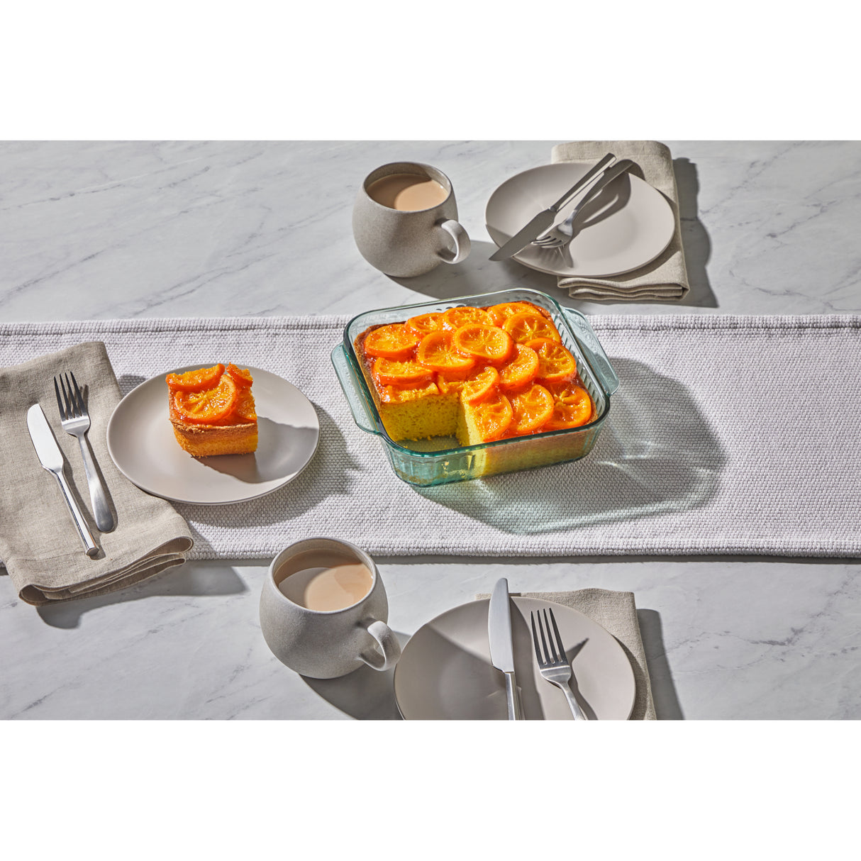 Table setting with a dish of orange cake and coffee cups on a marble surface