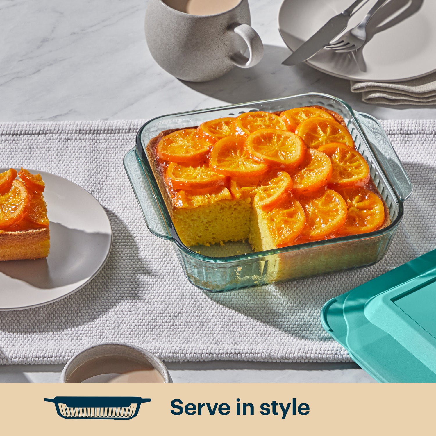 Glass dish with orange-topped dessert on a table setting with plates and cups.