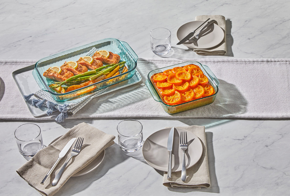 Dinner table setting with glass casserole dishes containing food on a marble surface.
