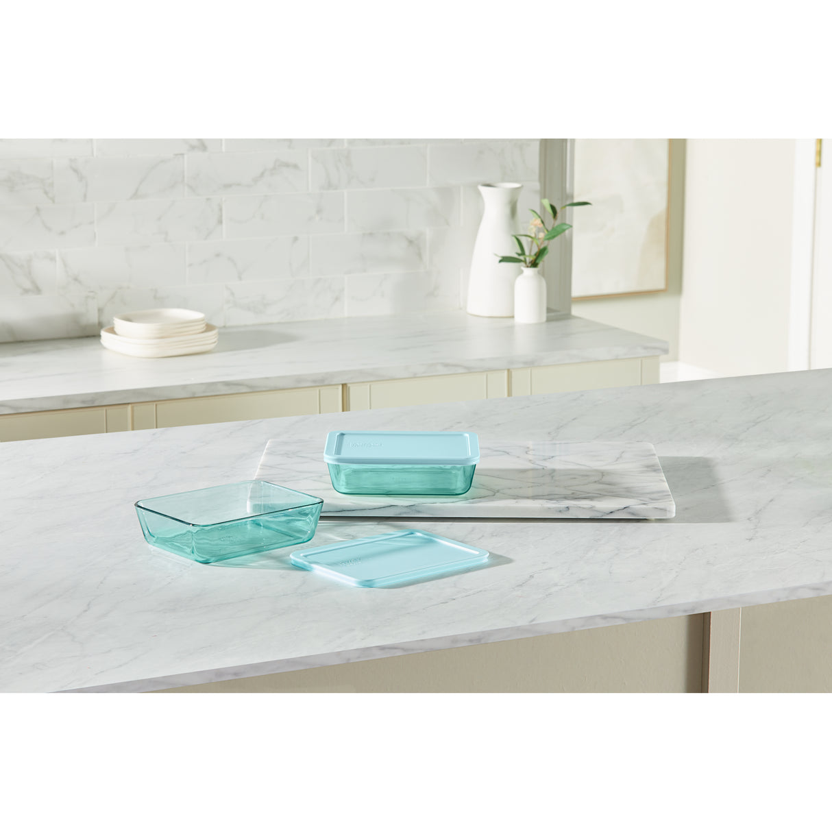Three turquoise glass containers on a marble countertop with a kitchen setting in the background.