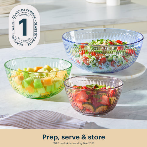 Three glass bowls filled with salad on a kitchen counter, with a brand logo in the corner.