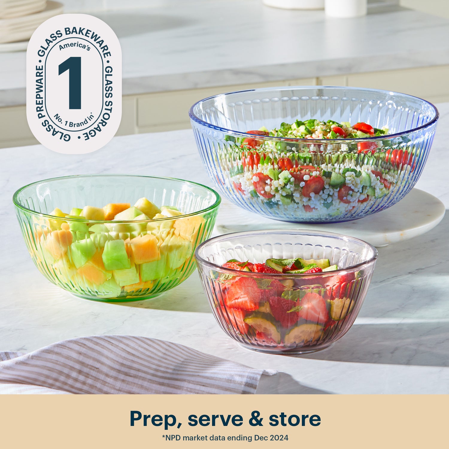 Three glass bowls filled with salad on a kitchen counter, featuring a brand logo in the corner.