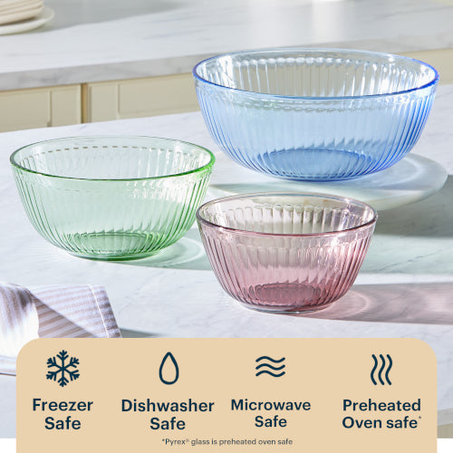 Three glass bowls in green, blue, and pink on a kitchen counter with safety icons below.