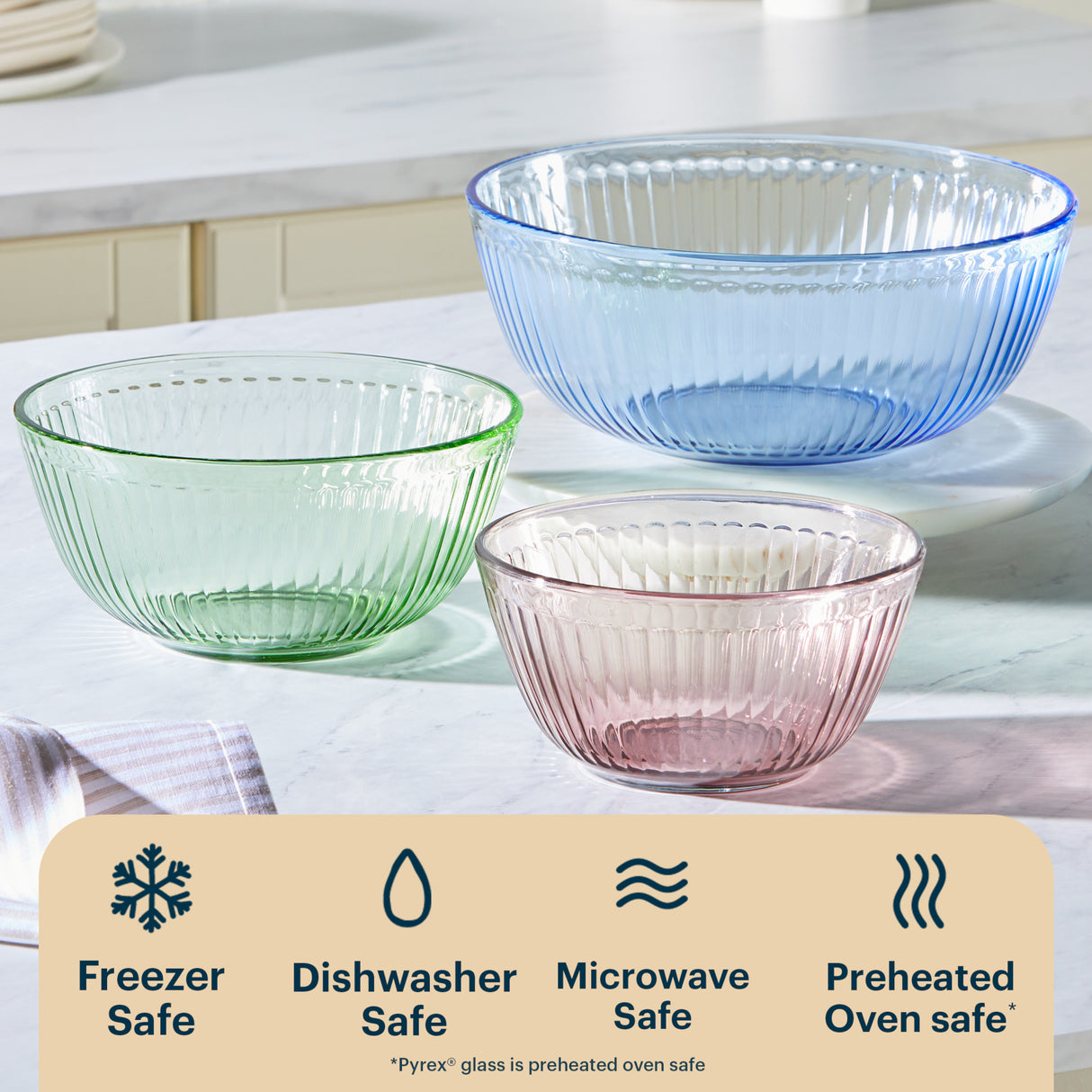Three glass bowls in green, blue, and pink on a kitchen counter with safety icons below.