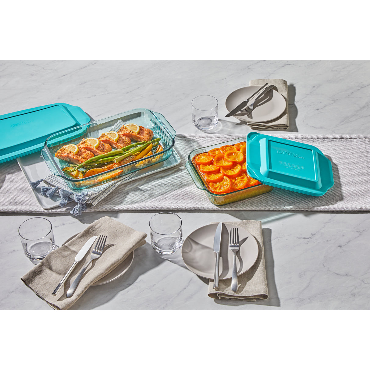 Glass food containers with turquoise lids on a marble table with a meal setup.