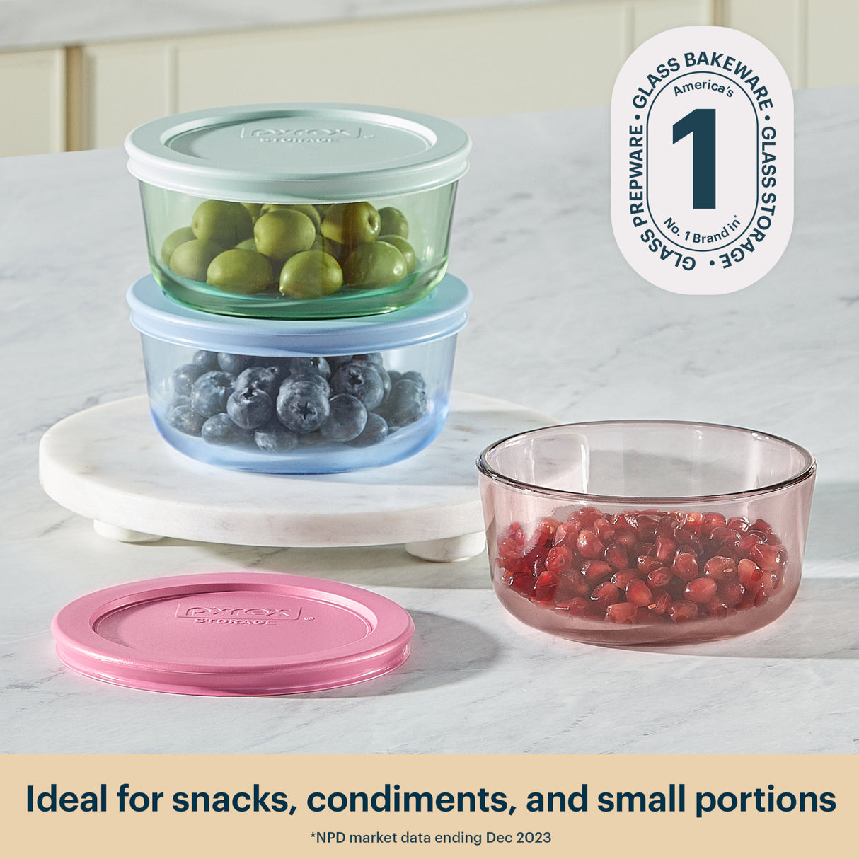 Set of glass food storage containers with lids on a marble surface, featuring the brand logo.