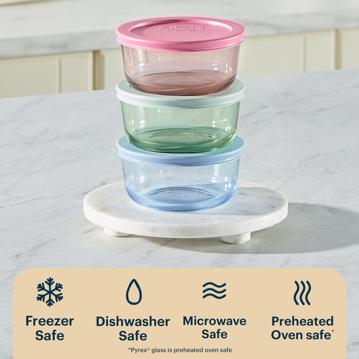 Stack of glass food containers with colored lids on a marble surface, featuring safety icons below.