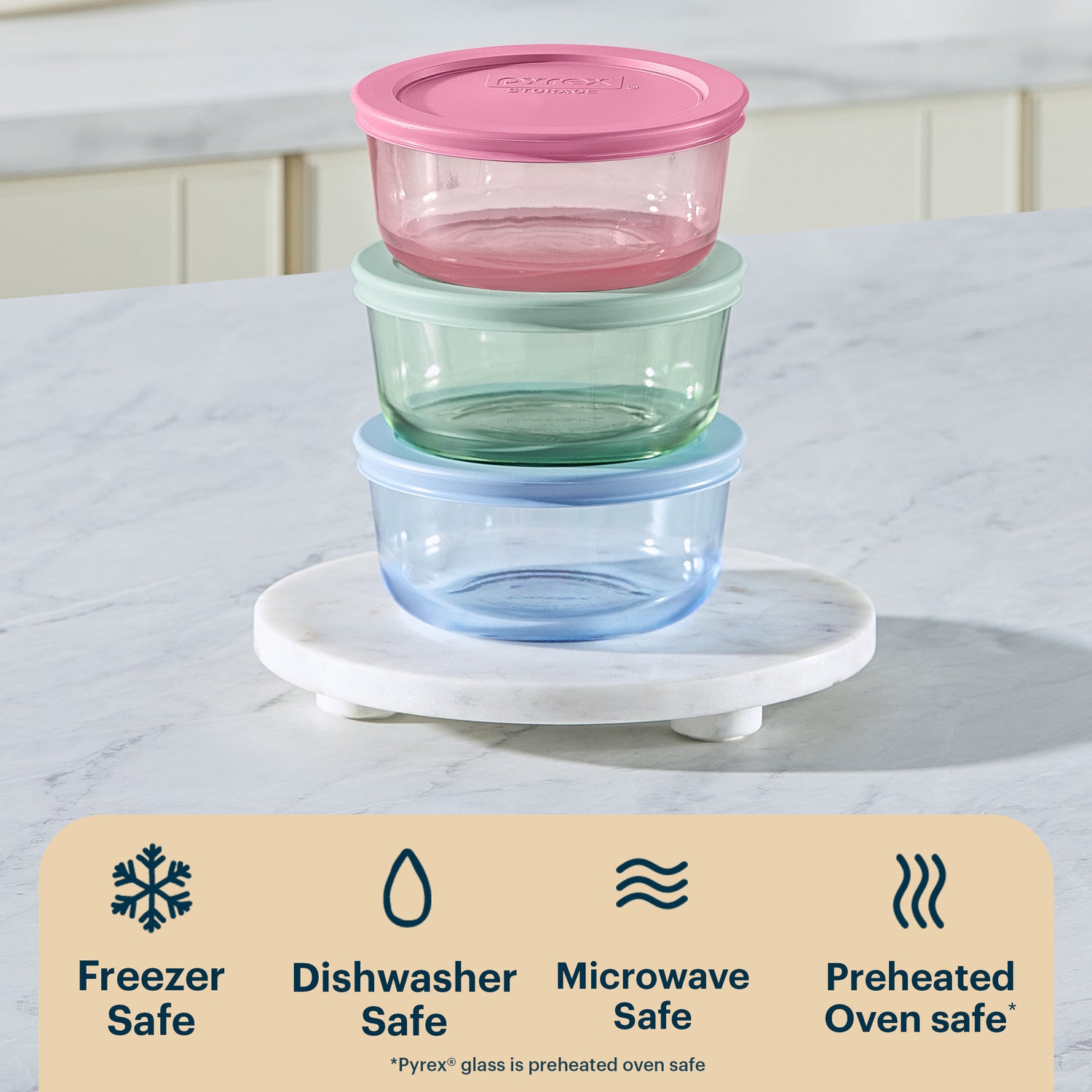 Stack of glass food containers with colorful lids on a marble surface, featuring Pyrex branding.