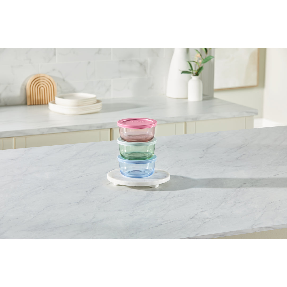 Stack of colorful glass containers on a white surface with a kitchen background