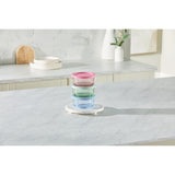 Stack of colorful glass containers on a white surface with a kitchen background