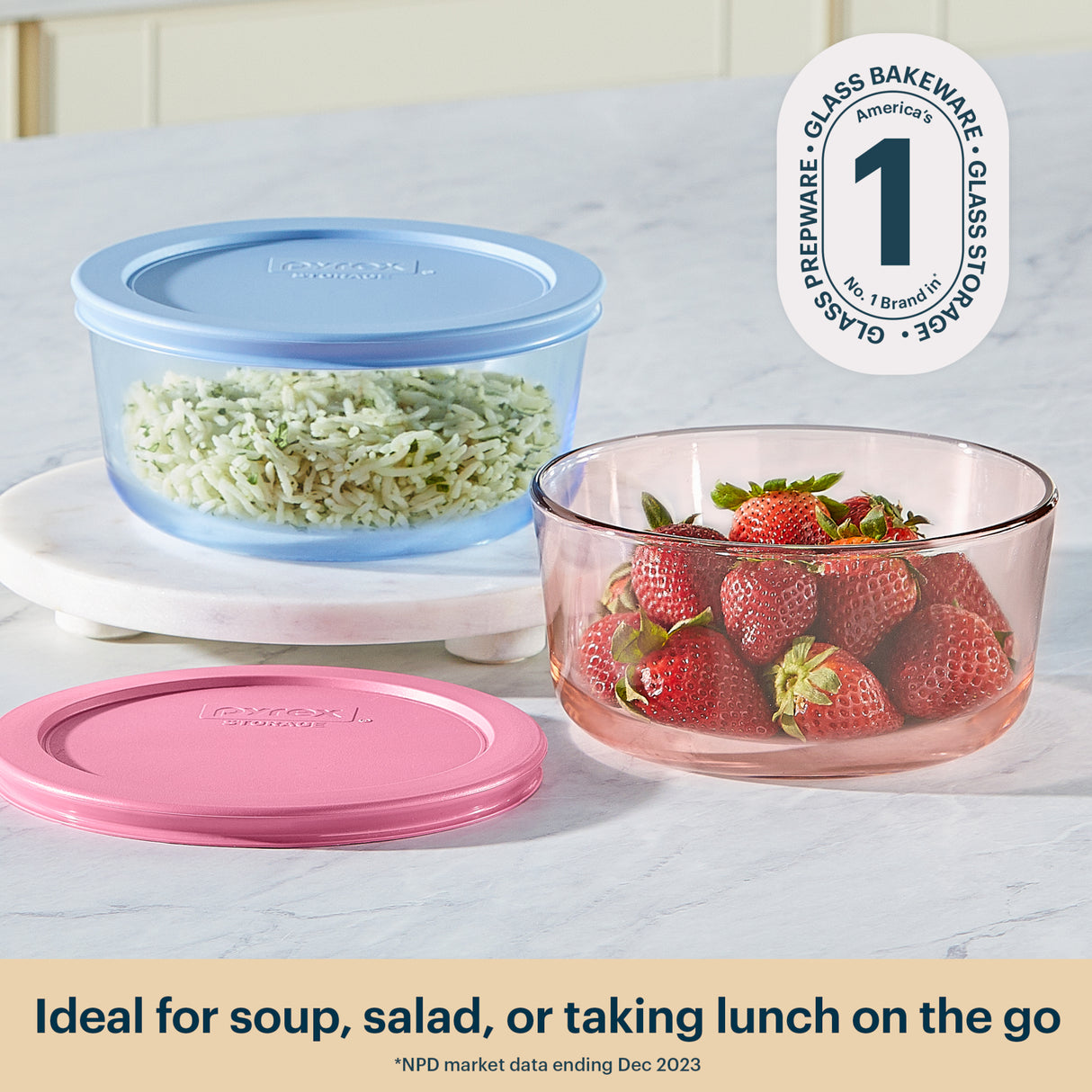 Glass bakeware set with pink and blue lids on a white surface, containing rice and strawberries.