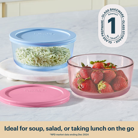 Glass food storage containers with lids containing rice and strawberries on a white surface.