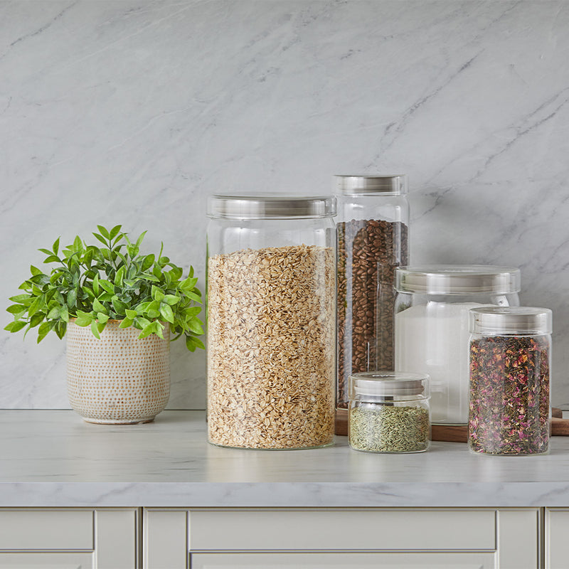 Set of glass jars with different contents on a kitchen counter with a marble wall background