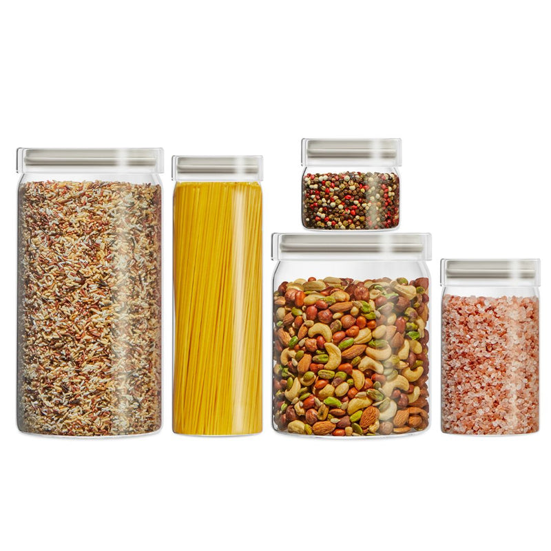 Set of glass storage jars with lids containing various dry goods on a white background