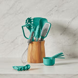 Teal kitchen utensils including a whisk, spatula, and measuring cups in a wooden holder on a marble countertop.