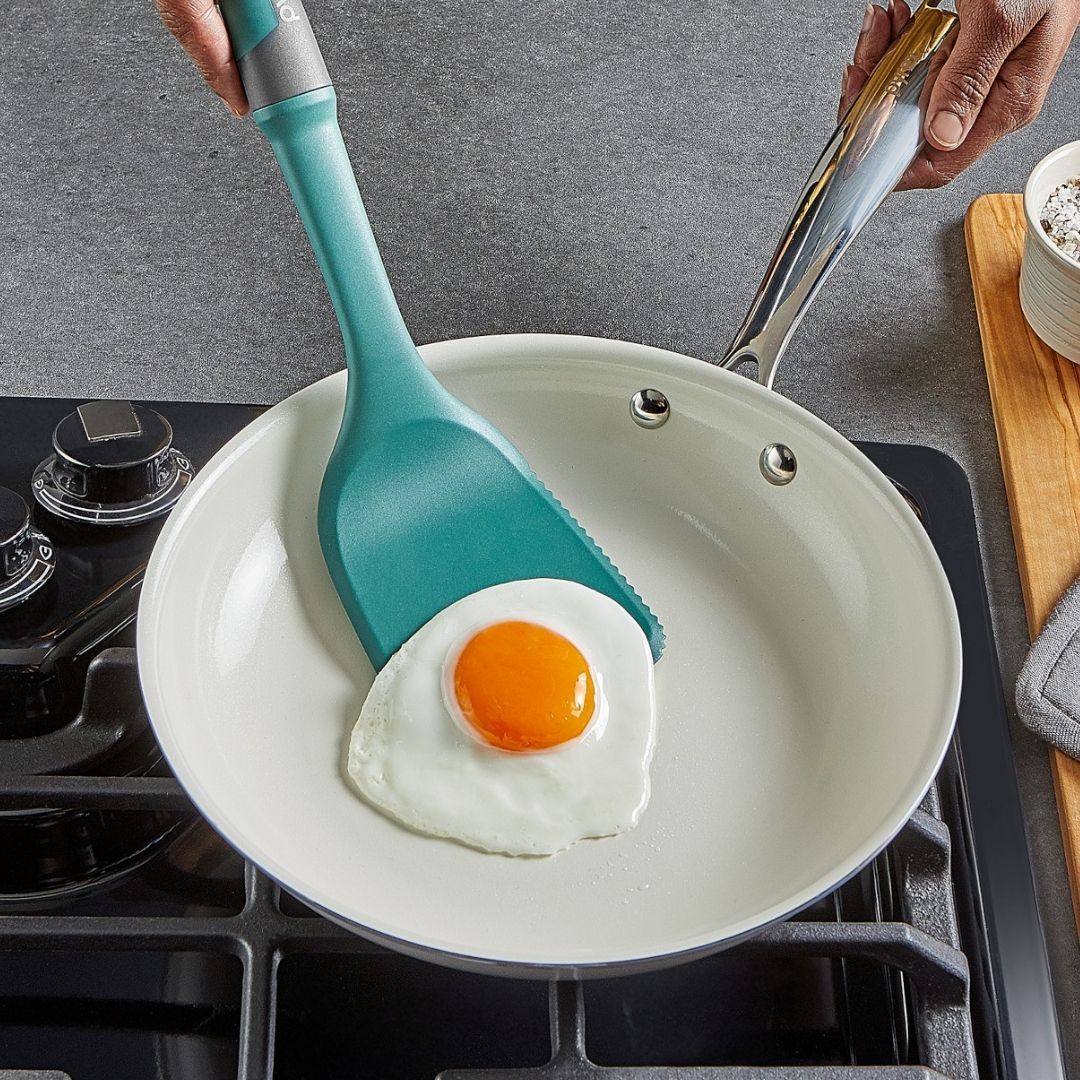 Teal spatula lifting a fried egg from a pan on a stove.