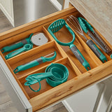Kitchen utensils including a whisk, spatula, and measuring cups in a wooden drawer organizer.