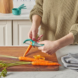 Person using a turquoise vegetable peeler on carrots on a wooden cutting board in a kitchen.