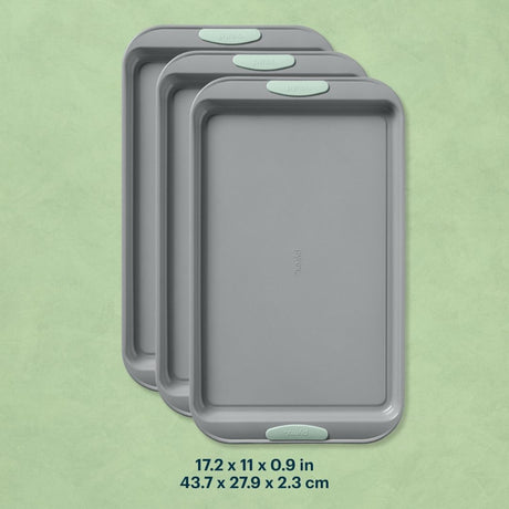 Three gray baking trays with green handles on a light green background