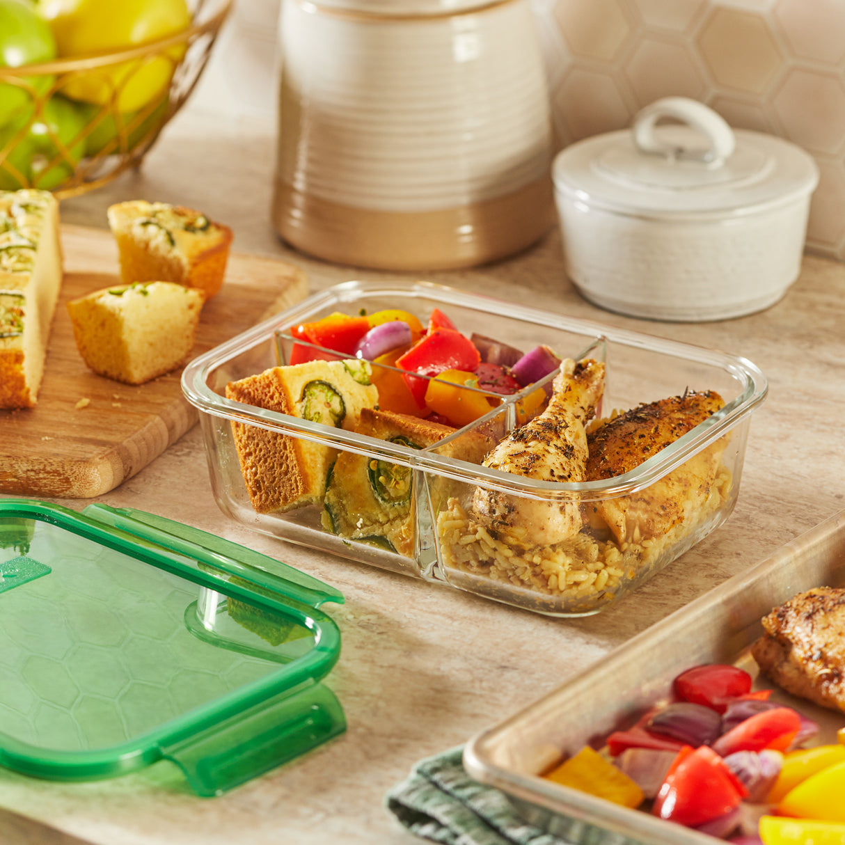 Glass food container with compartments on a wooden table with bread and vegetables.