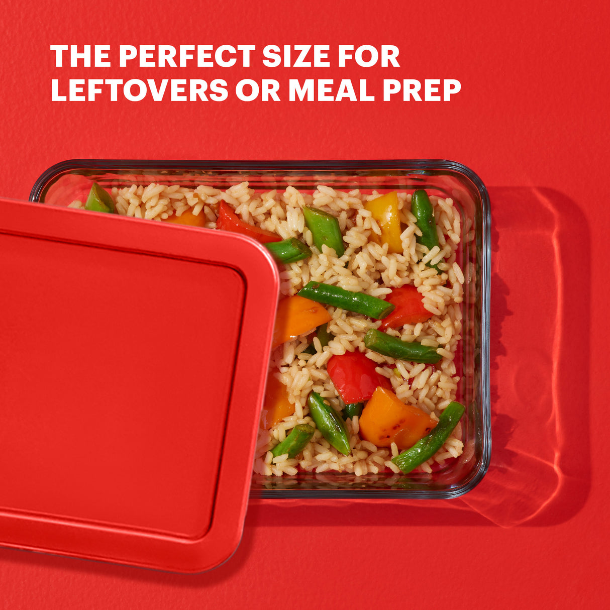 Glass food container with lid filled with rice and vegetables on a red background